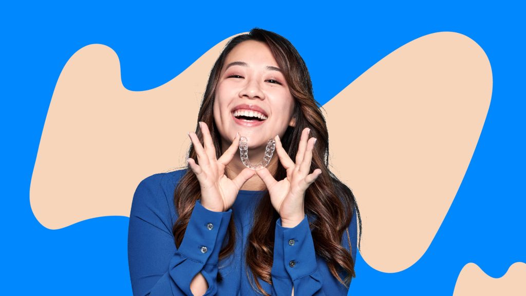 A lady smiling while holding up a pair of aligners